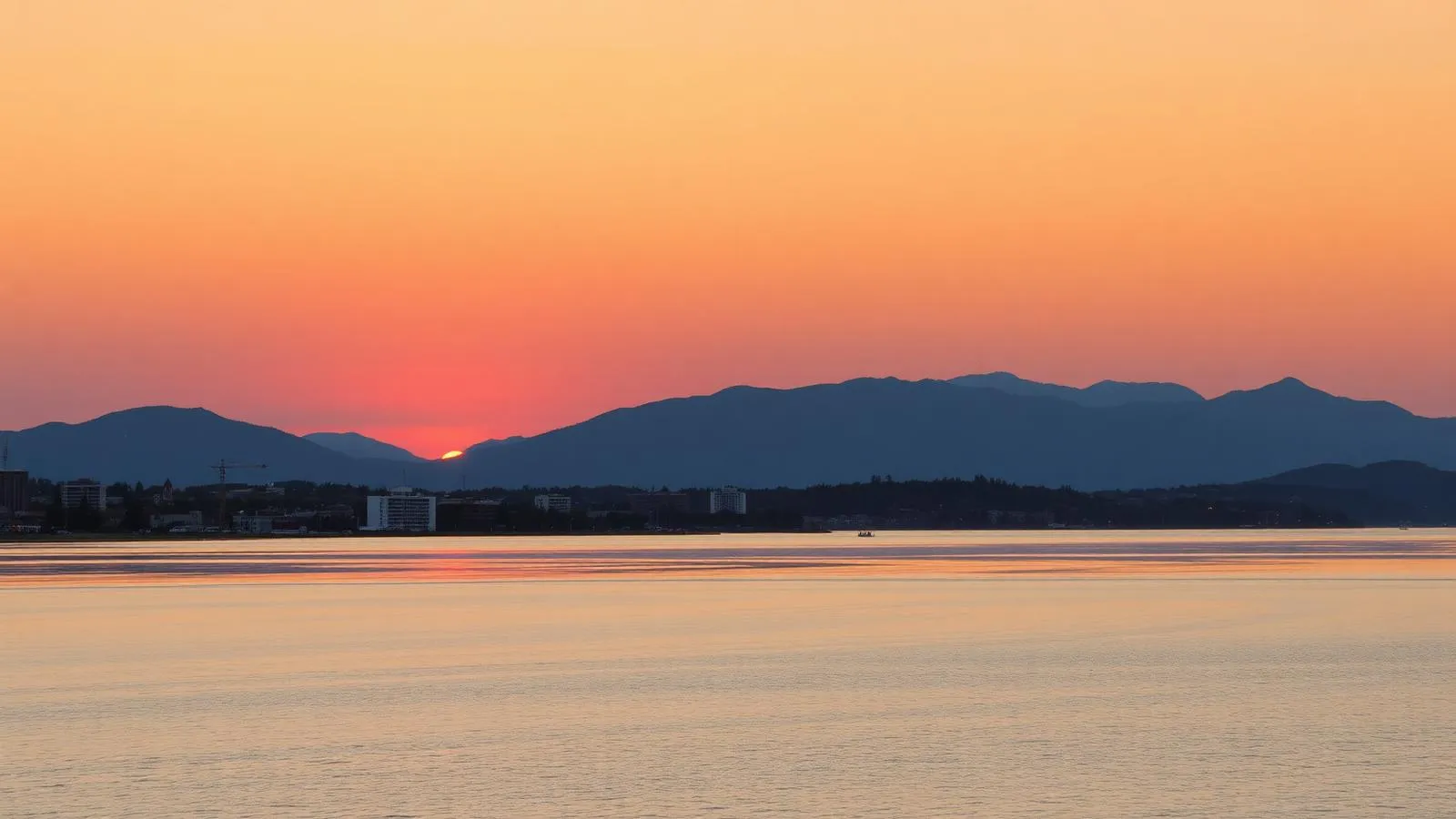Coucher de soleil orange sur le lac Mégantic avec le centre-ville reconstruit et les montagnes en arrière-plan